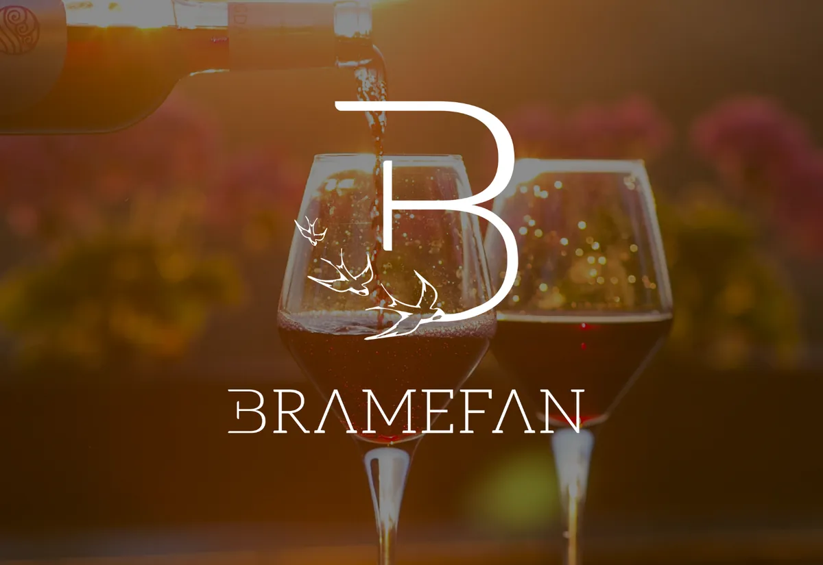 Logo Bramefan, monogramme B aux hirondelles, en blanc sur une photo de verres de vin au coucher du soleil