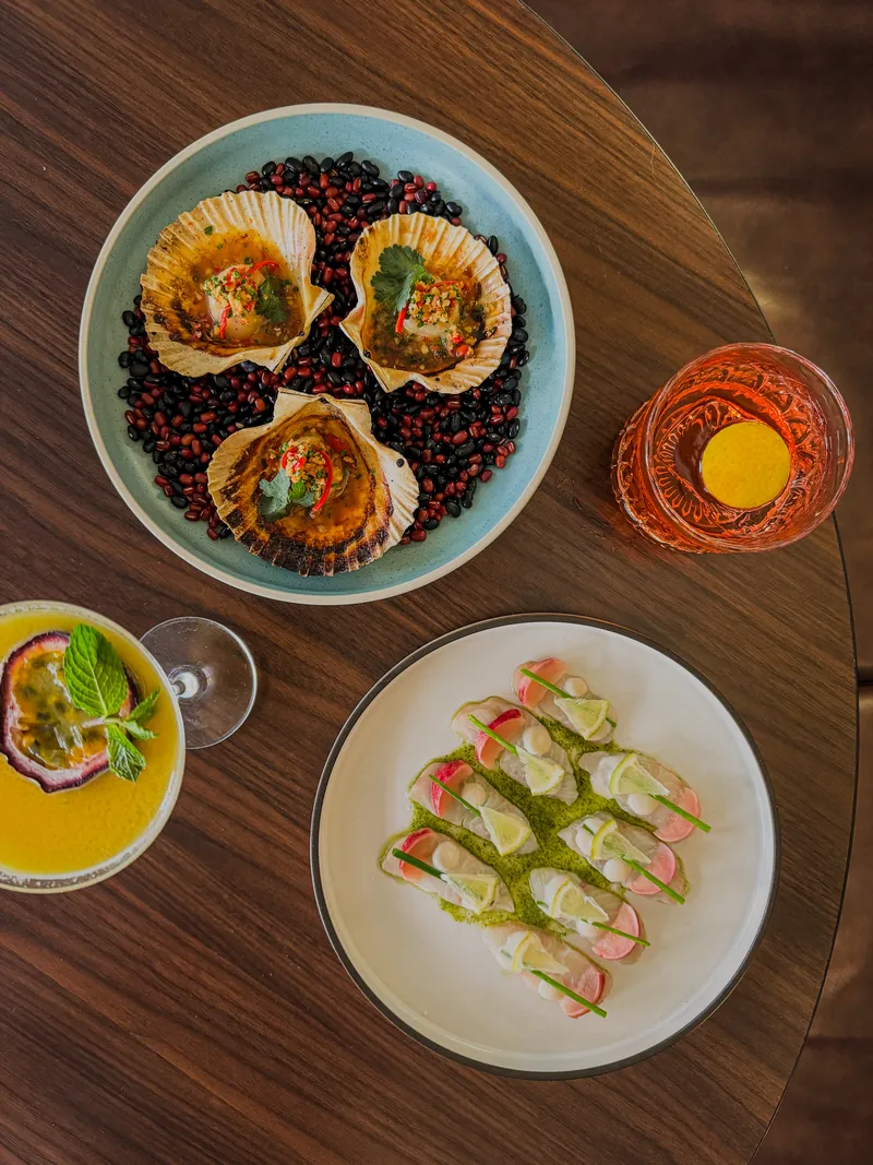 Vue du dessus d'une table de restaurant : coquilles Saint-Jacques, carpaccio de poisson et deux cocktails