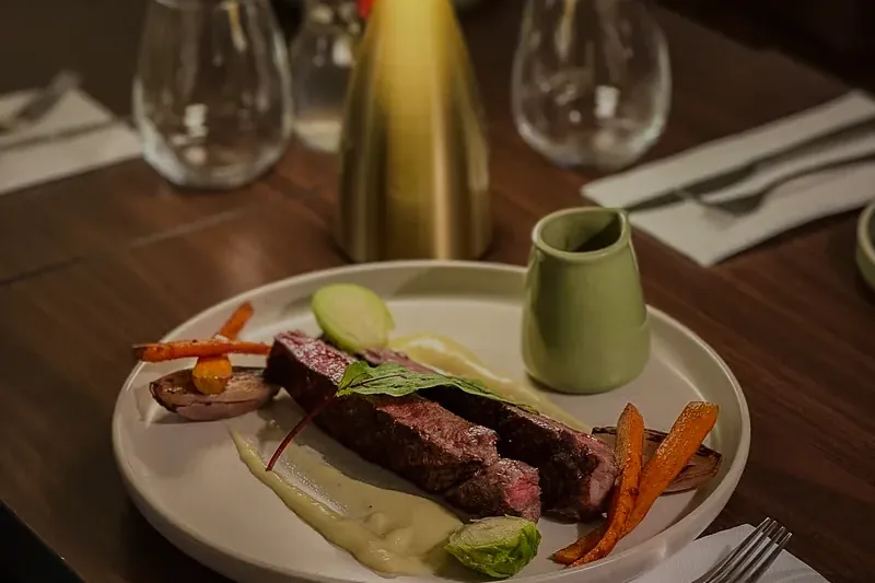 Pièce de bœuf, carottes rôties et purée sur une table dressée, avec une lampe en laiton