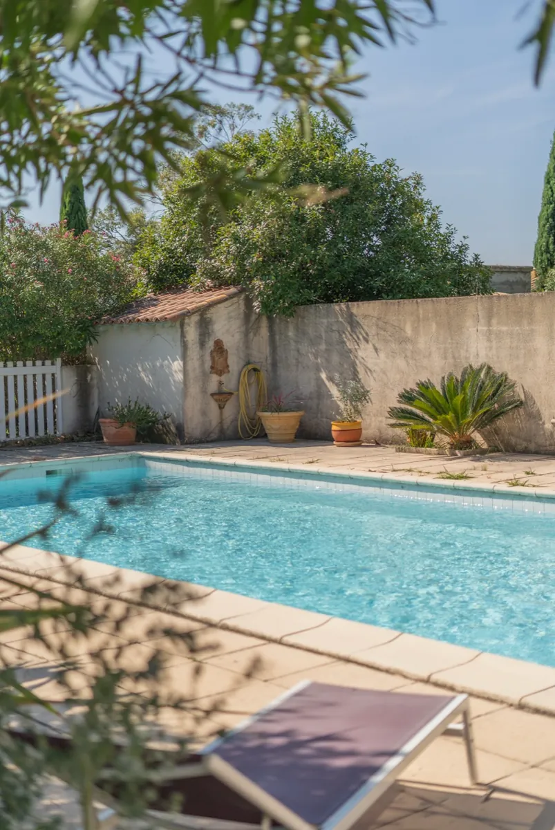 Piscine avec fontaine murale et pots de fleurs, maison Orpi Belle Pierre à Beaucaire