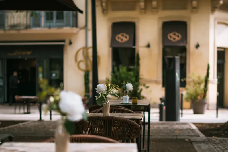 Terrasse de restaurant avec tables, chaises tressées et fleurs devant une façade ancienne