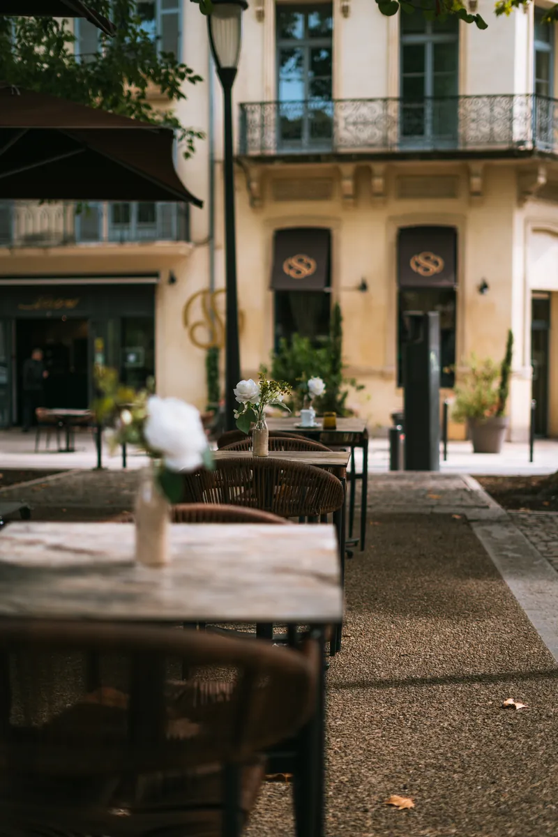 Terrasse de restaurant avec tables, chaises tressées et fleurs devant une façade ancienne